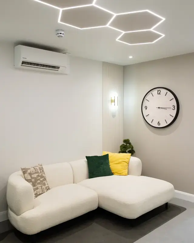 A sofa beneath hexagon ceiling lights and a large wall clock